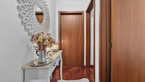 Un corridoio con una porta in legno, un tavolino consolle bianco con un vaso di fiori e uno specchio decorativo appeso al muro.