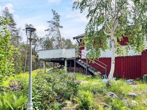 A red wooden structure with a balcony, surrounded by greenery and a street lamp.