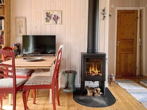 Ein gemütliches Zimmer mit Holzboden, einem Esstisch mit Stühlen, einem Fernseher und einem Kaminofen.