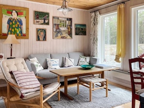 A cozy room with a wooden ceiling, a grey sofa, a wooden table, and a chair. - 4 Star Holiday Home in Blido (Blidö)