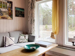 A cozy room with a sofa, a table with a bowl, a window with curtains, and a painting on the wall.
