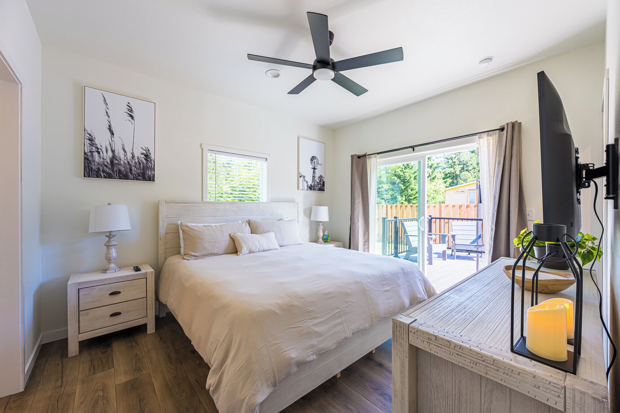 A bedroom with a bed, nightstands, a ceiling fan, and a view of the outdoors.