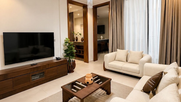 En moderne stue med et fladskærms-tv, et træbord, en beige sofa og en lysekrone.