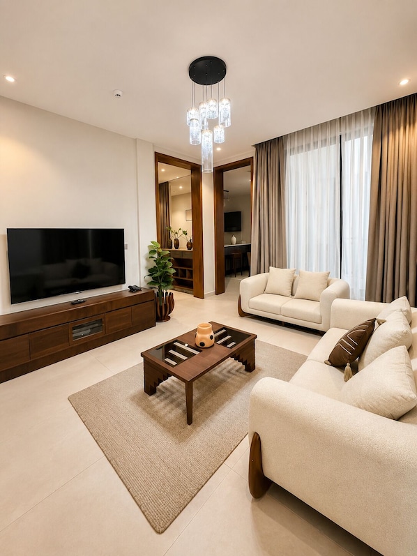 A modern living room with a flat-screen TV, a wooden coffee table, a beige sofa, and a chandelier.
