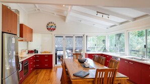 A modern kitchen with wooden cabinets, a dining table, and a large window. - Casa Lagoona - Coastal Retreat by the Beach (Quindalup)