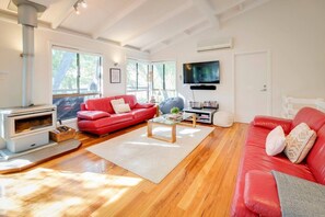 Ein modernes Wohnzimmer mit einem roten Sofa, einem Glastisch, einem Kamin und einem an der Wand befestigten Fernseher.
