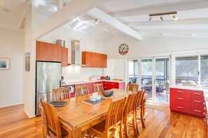 Una cocina moderna con armarios de madera, un refrigerador de acero inoxidable y una zona de comedor con mesa y sillas de madera.