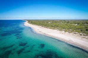 Vista aérea de una playa con aguas turquesas cristalinas, una orilla de arena y abundante vegetación al fondo.