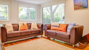 A living room with two brown leather sofas, a beige rug, and large windows with a view of trees. - Casa Lagoona - Coastal Retreat by the Beach (Quindalup)