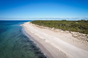 En strand med klart vand, sandet bredde og frodig bevoksning.