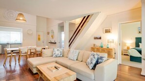 Un saló modern amb un sofà modular, una taula baixa de fusta i una escala que condueix a un altre nivell.