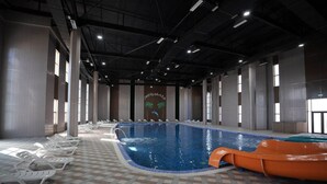An indoor swimming pool with lounge chairs, a slide, and a tiled floor. - Arda Oasis (Khiva)