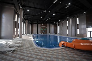 An indoor swimming pool with lounge chairs, a slide, and a tiled floor. - Arda Oasis (Khiva)