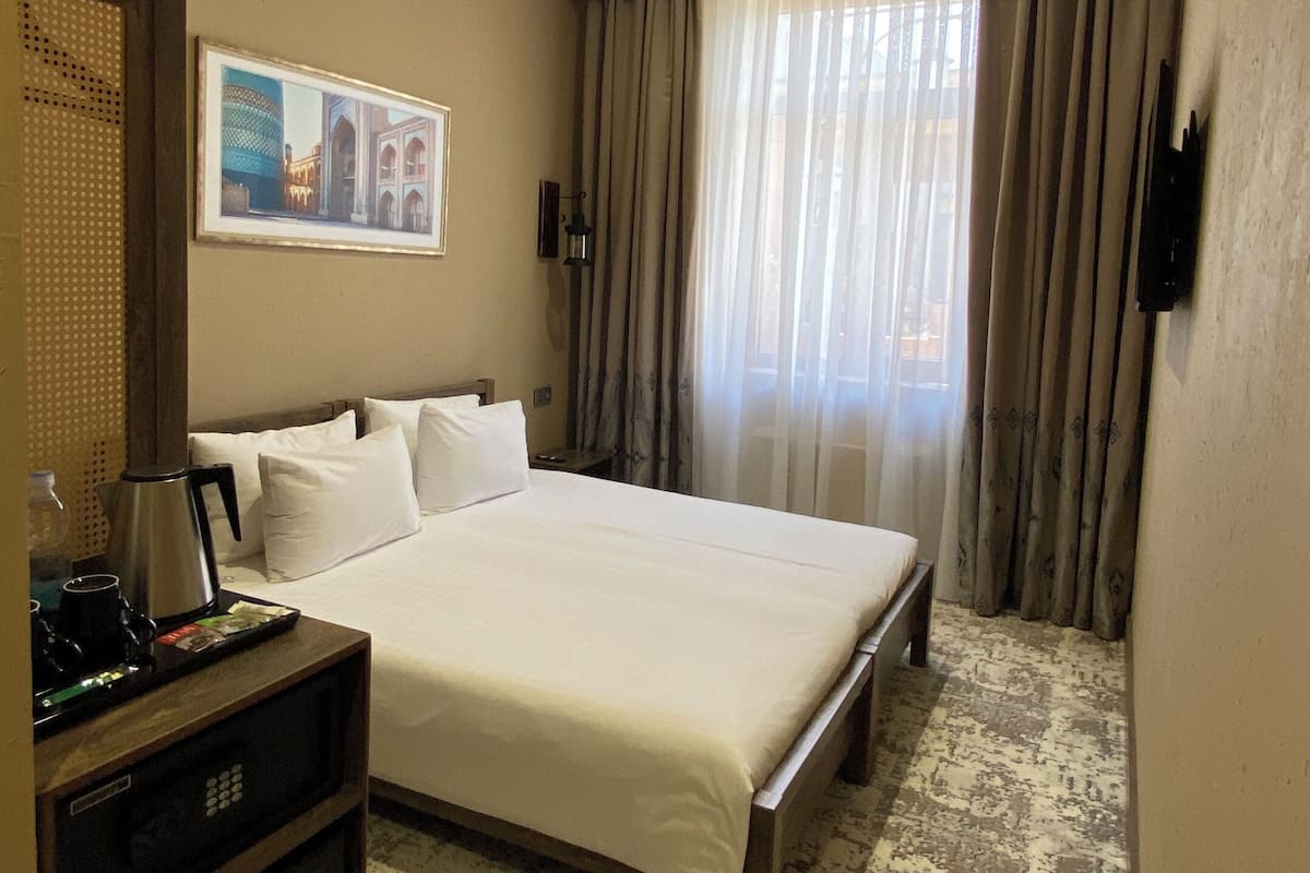 A hotel room with a large bed, a television, a minibar, a picture on the wall, and a window with curtains.