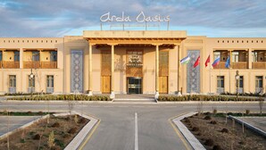 A hotel entrance with a sign reading 'Arda Oasis,' multiple flags, and a symmetrical facade with columns and decorative elements. - Arda Oasis (Khiva)