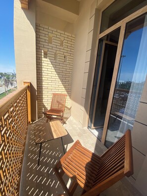 A balcony with a wooden chair, a small table, and a view of the cityscape through a glass door. - Arda Oasis (Khiva)