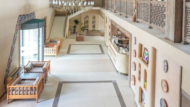 A spacious lobby with a grand chandelier, a staircase, and a reception desk. - Arda Oasis (Khiva)