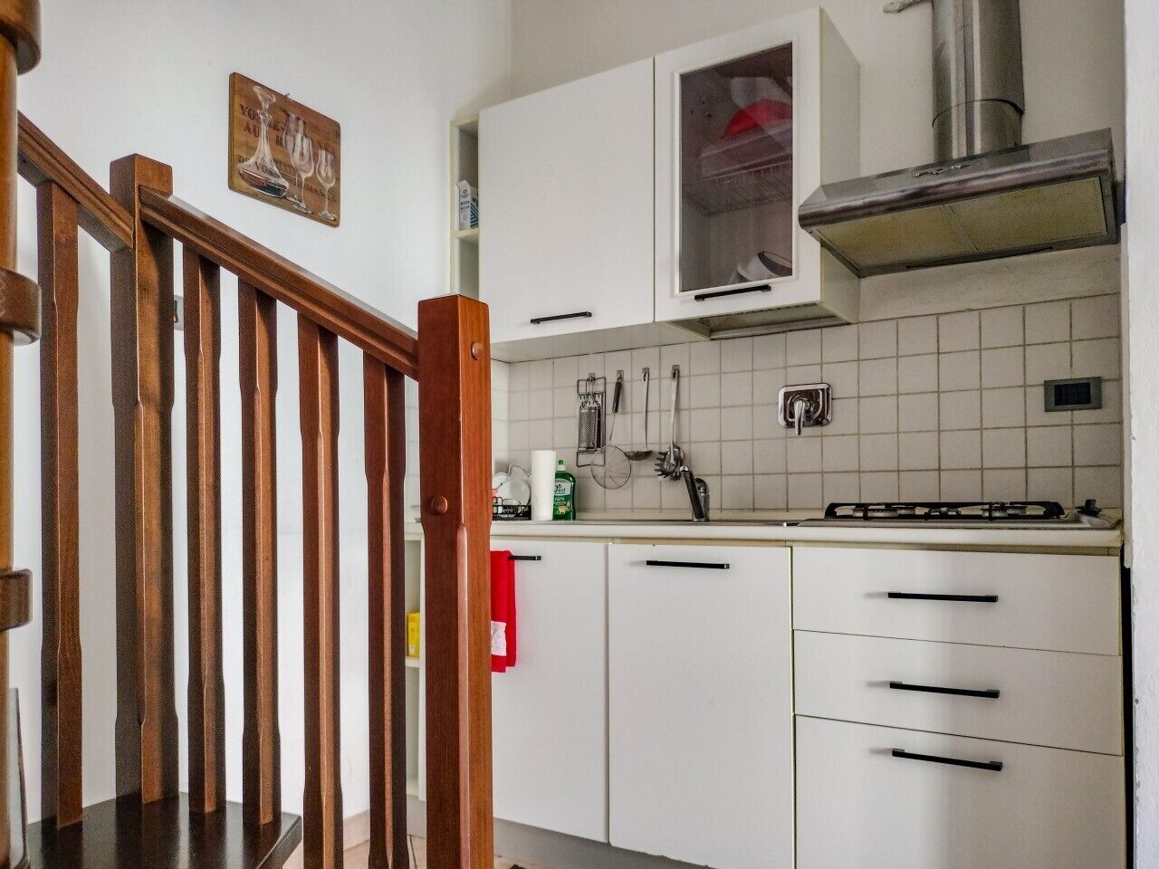 A kitchen with white cabinets, a stainless steel range hood, and a wooden staircase.