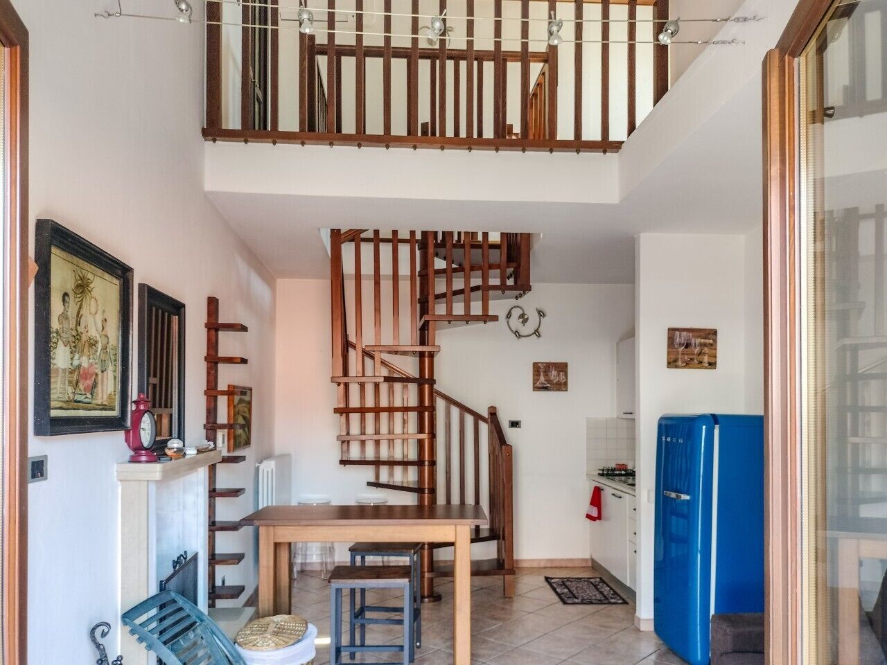 A kitchen with a wooden staircase, a dining table, and a blue refrigerator.