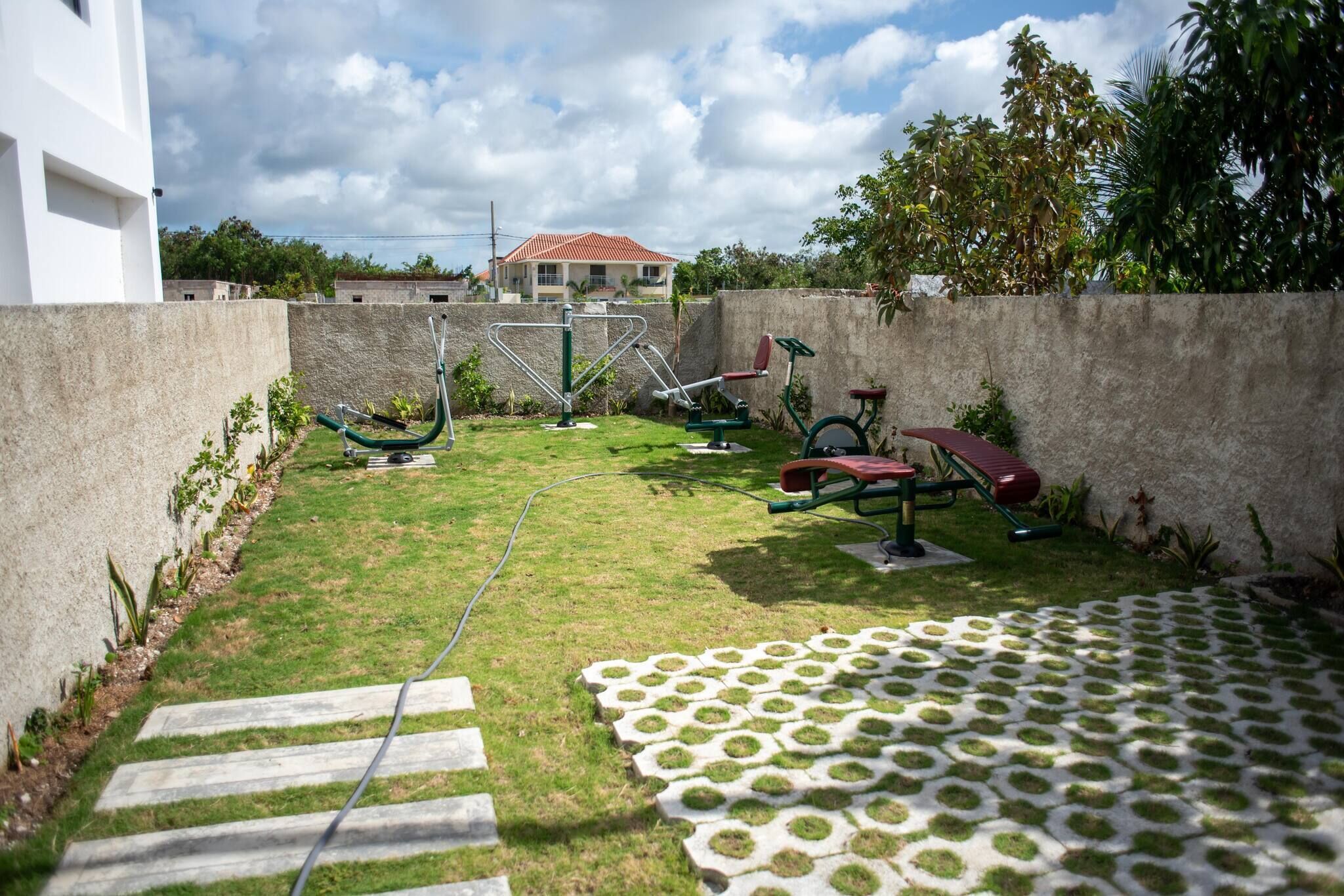 A backyard with outdoor exercise equipment, a paved area with stepping stones, and a house in the background.