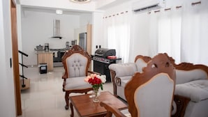 A modern living room with a sofa, armchairs, a dining table, and a kitchen in the background.