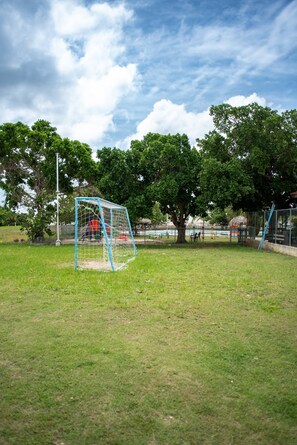 A soccer goal in a park with trees and a fence in the background.