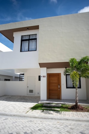 A modern two-story house with a number '03' on the door, a small tree, and a paved courtyard.