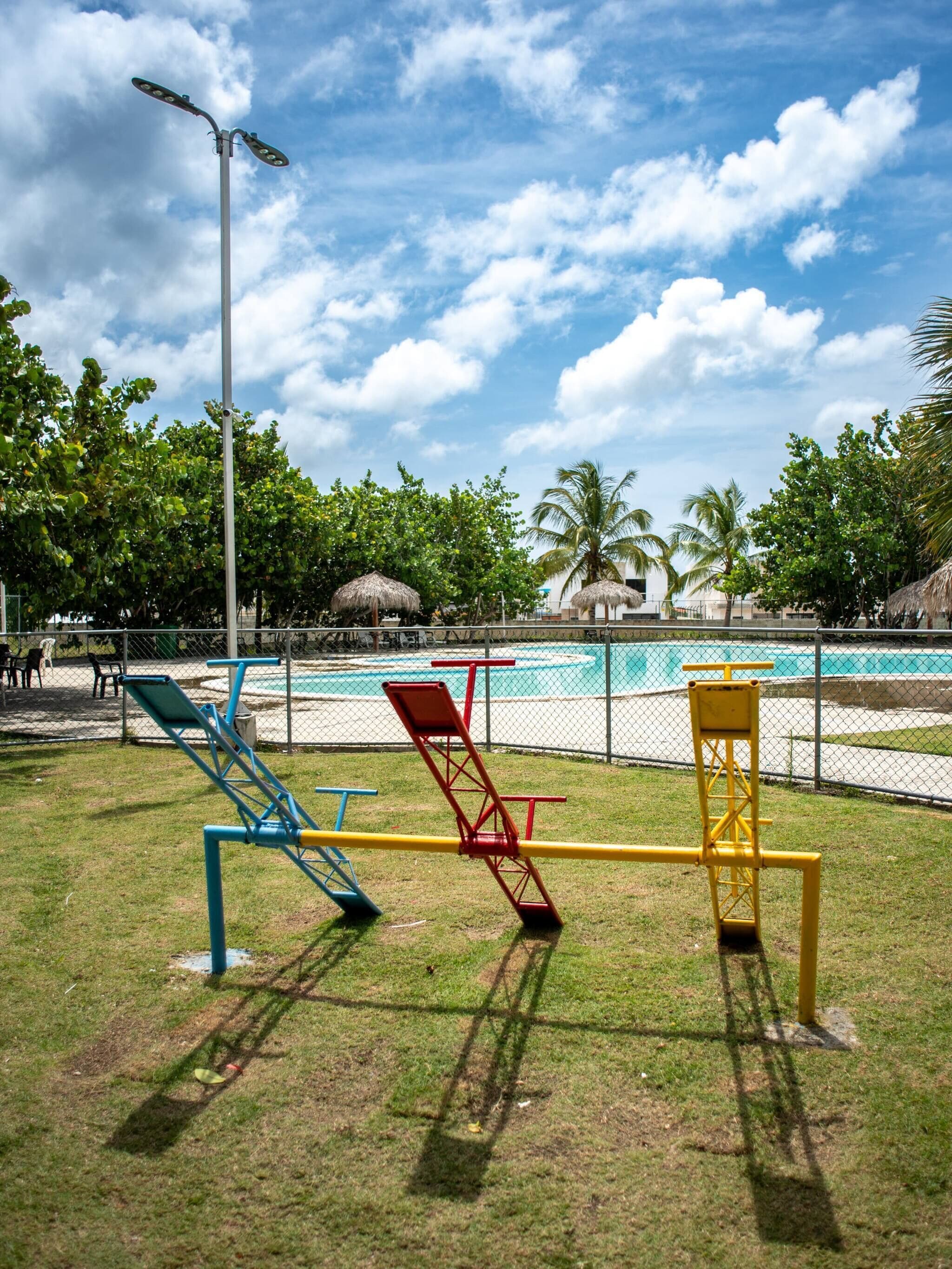 Un terrain de jeux équipé d’installations d’exercice, une piscine et des palmiers.