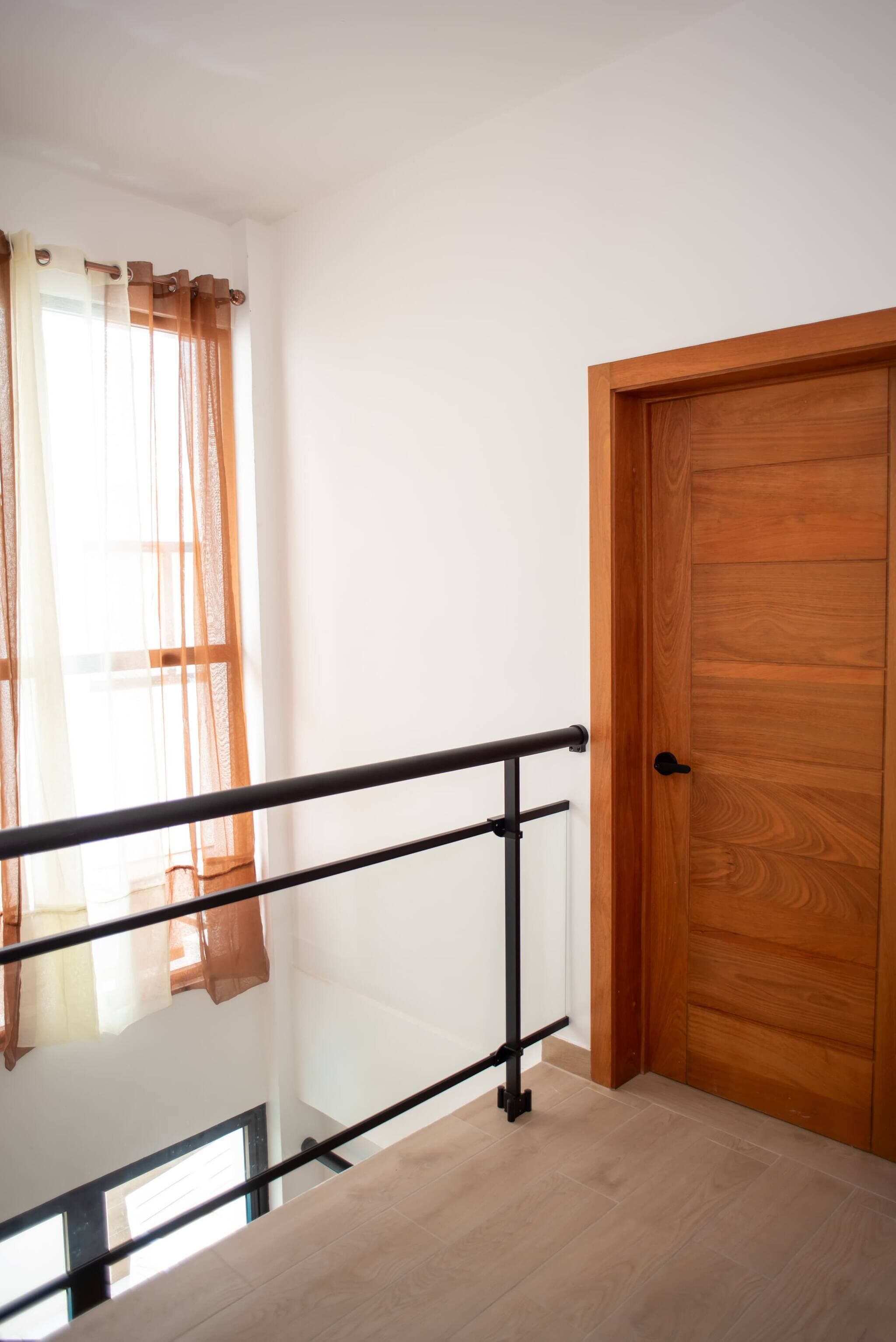 Een houten deur, een glazen balustrade en een raam met transparante gordijnen.