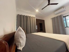 Ein Schlafzimmer mit einem Bett, einem Deckenventilator, einer Klimaanlage und einem Vorhangfenster.