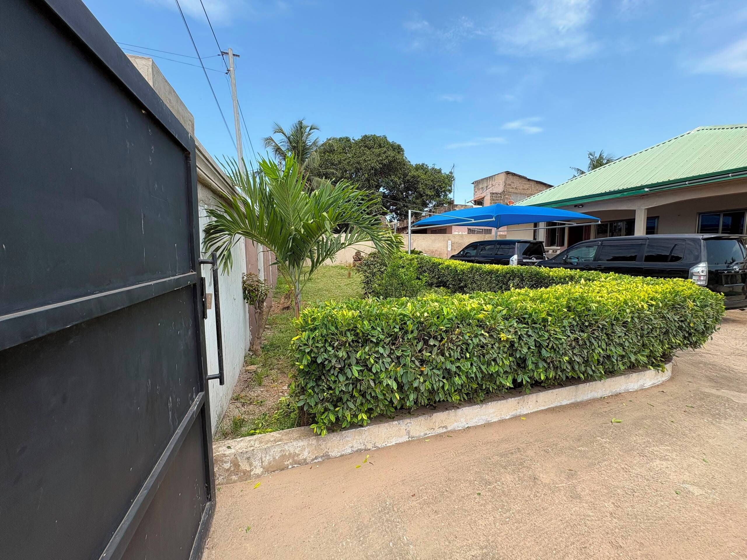 Un espace de stationnement avec une voiture noire, un parasol bleu et un bâtiment doté d’un toit vert.