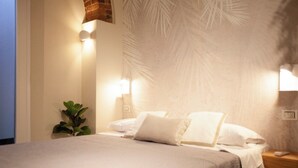 A neatly made bed with white linens, a small bedside plant, and wall-mounted lights.
