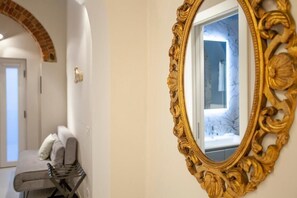 Un pasillo con un banco, un espejo con un marco dorado ornamentado y una puerta que da a un baño.