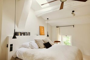 Une chambre à coucher comprenant un lit, un ventilateur de plafond, une fenêtre et un luminaire fixé au mur.