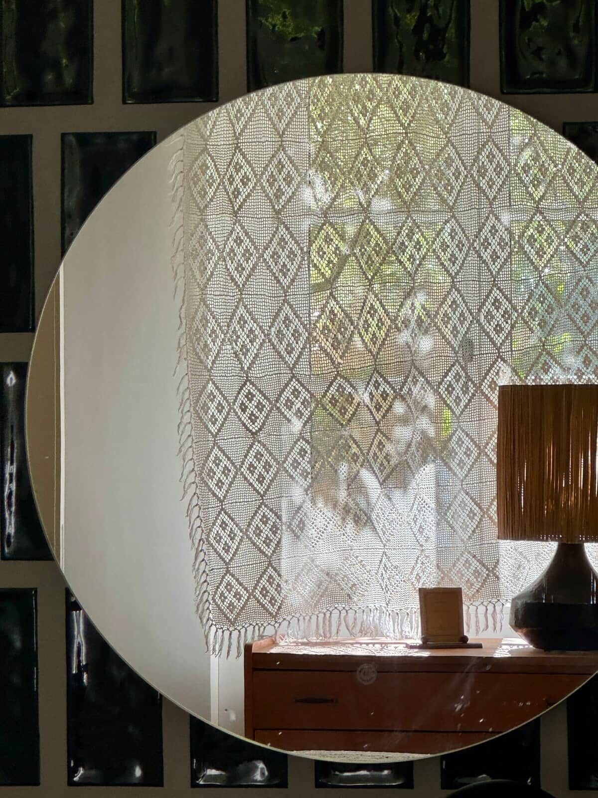 A room with a large round mirror, a wooden side table, and a patterned curtain.