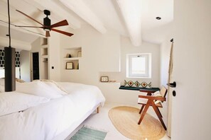 A bedroom with a bed, a desk, a chair, a ceiling fan, and a window.