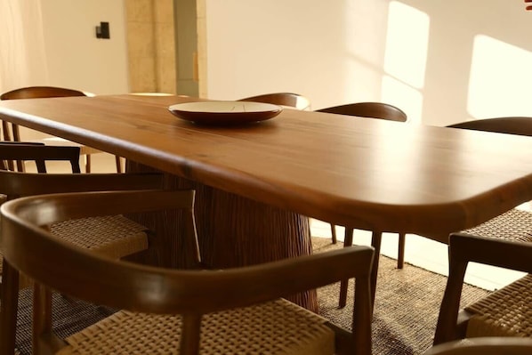 A wooden dining table with chairs, a woven chair back, and a woven floor mat.