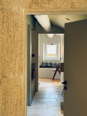 A hallway leading to a room with a window, a door, and a small table.