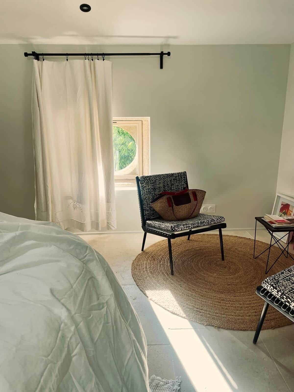 A bedroom with a bed, a chair, a small table, a window with a view, and a curtain.