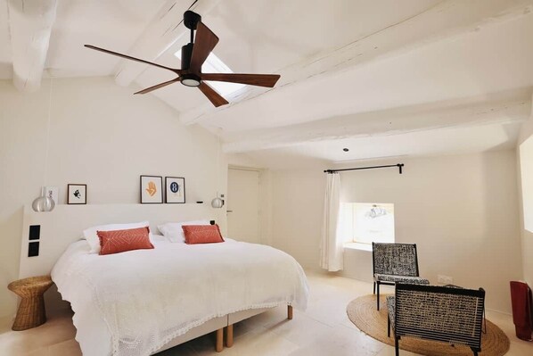 Une chambre à coucher avec un lit, un ventilateur de plafond, une chaise et une fenêtre.