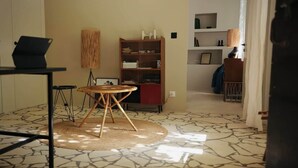 Een kamer met een ronde houten tafel, een boekenplank, een lamp en een vloer met een patroon.