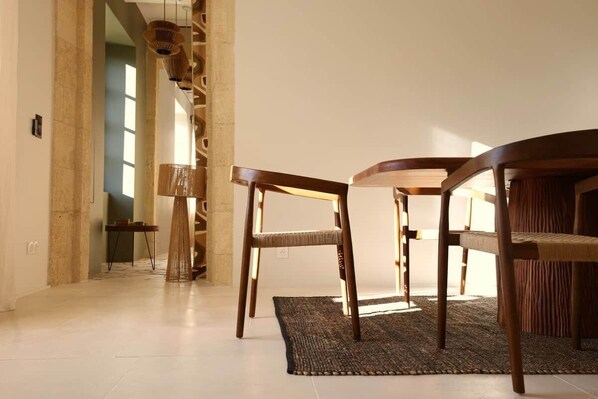 A modern interior with a dining area featuring a round table and two chairs, a woven floor rug, and a tall, slender lamp.