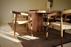 A round wooden table with woven chairs, a woven rug, and a wall-mounted light fixture. - Louna room (Saint-Victor-la-Coste)