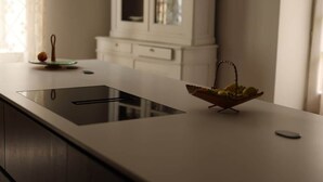 Une cuisine moderne avec une plaque de cuisson intégrée, un panier de fruits et un meuble en arrière-plan.