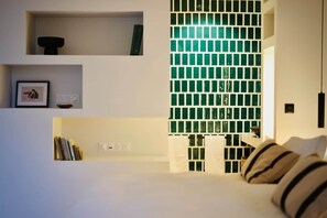 A modern bedroom with a white bed, a bookshelf, and a wall with green glass tiles.