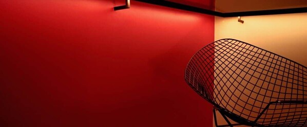 Una parete rossa, una sedia in filo nero e un lampadario.