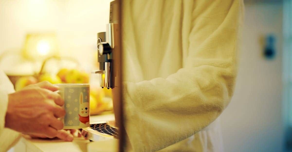 A person using a coffee machine, a cup, and a kitchen counter.