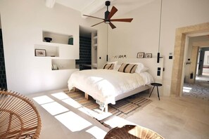 Une chambre à coucher comprenant un lit, un ventilateur de plafond, des étagères intégrées et donnant sur un couloir.