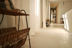 A corridor with a wicker chair, a table, and a lamp.