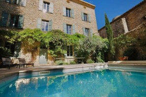 Un bâtiment en pierre doté d’une piscine, d’un espace extérieur aménagé et de verdure.